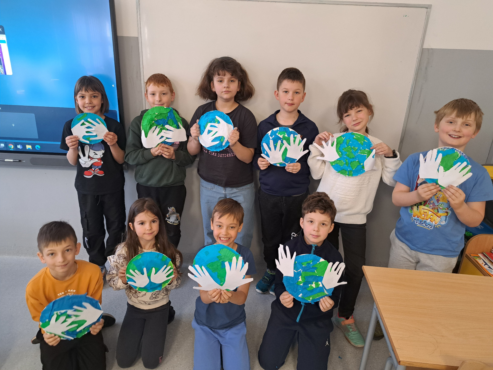 Uczniowie pozują z pracami przedstawiającymi Ziemię