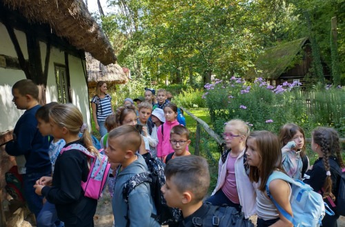 Uczniowie podczas zwiedzania skansenu stoją przed zabytkową chatą