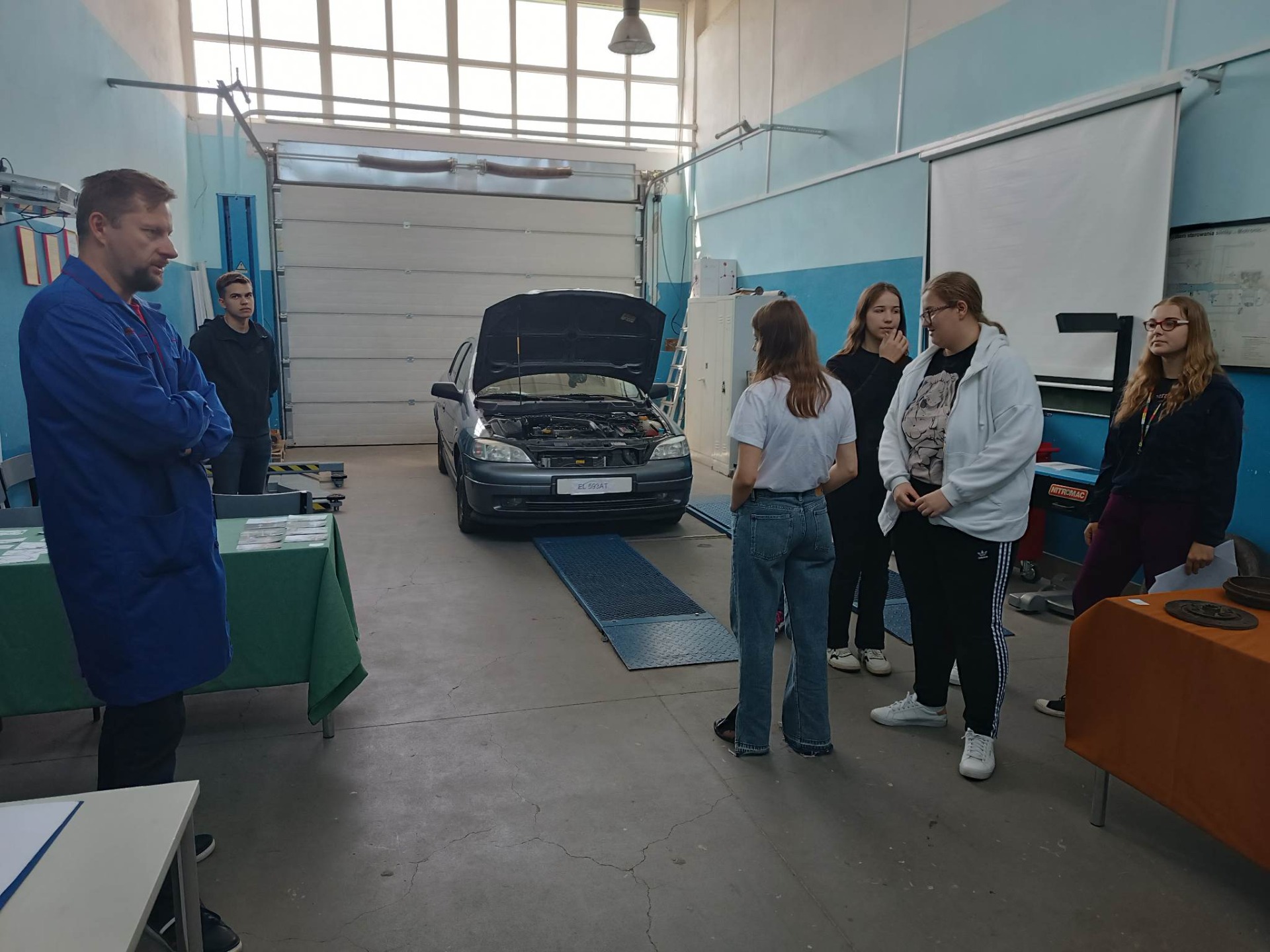 Grupa uczennic rozwiązuje zadanie dotyczące marek samochodów, przed nimi stoi prowadzący nauczyciel