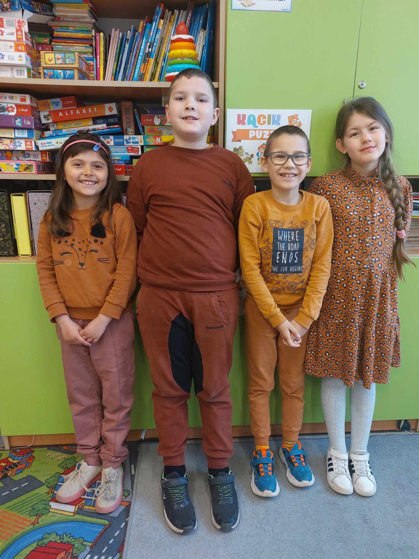 4 uczniów młodszych klas ubranych na brązowo pozuje na stojąco do zdjęcia
