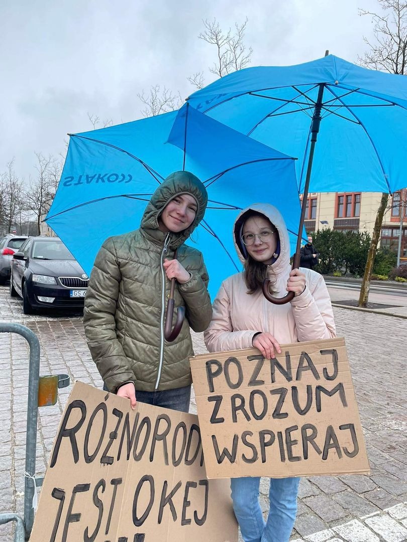 Uczennice na placu z niebieską parasolką i plakatem 3