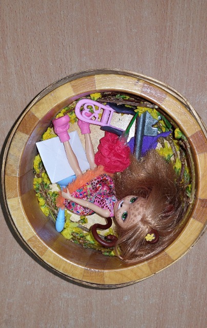 Okrągłe pudełko, w którym znajdują się kwiaty i lalka.