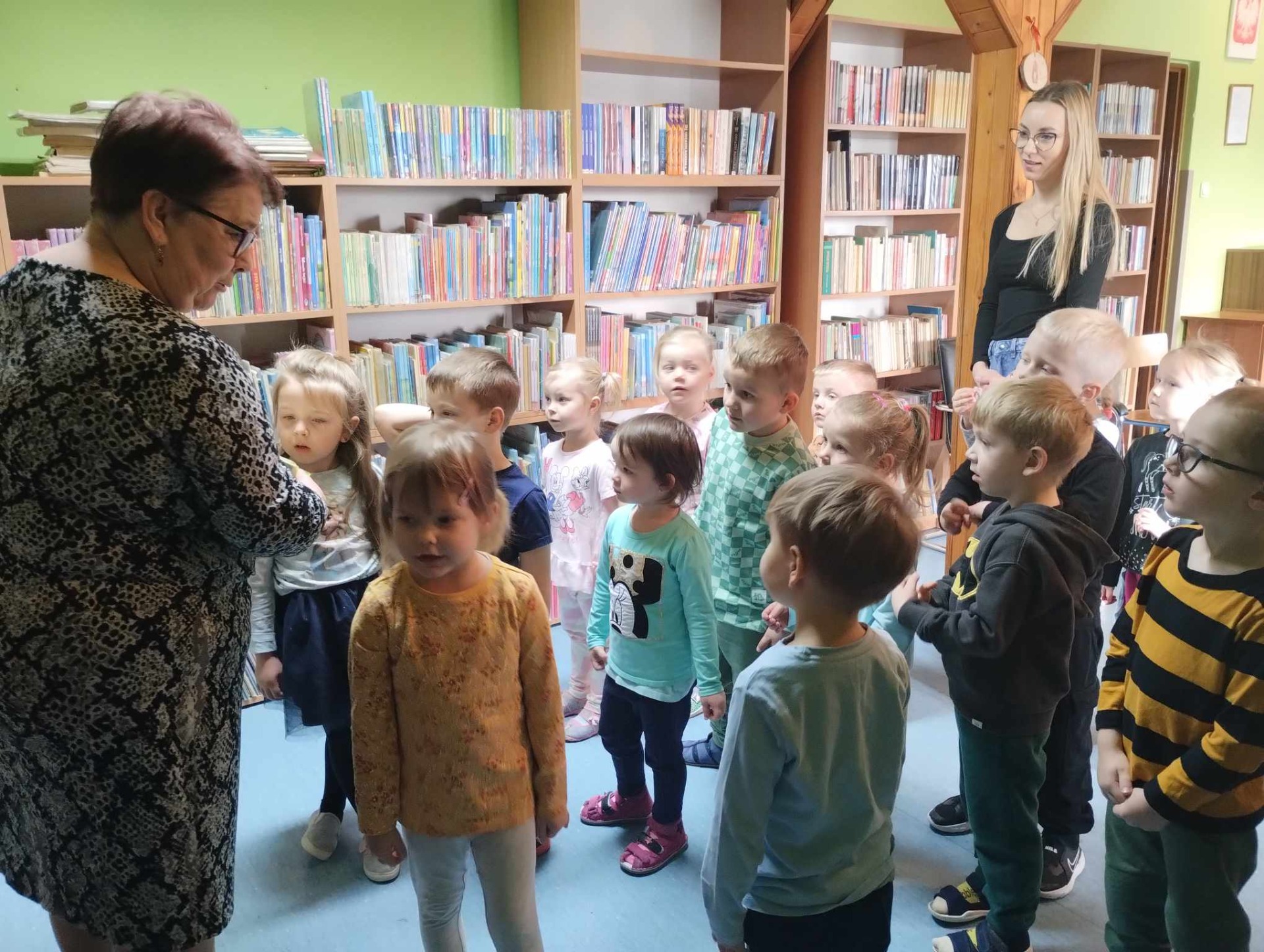 Grupa przedszkolaków zwiedza szkolną bibliotekę.