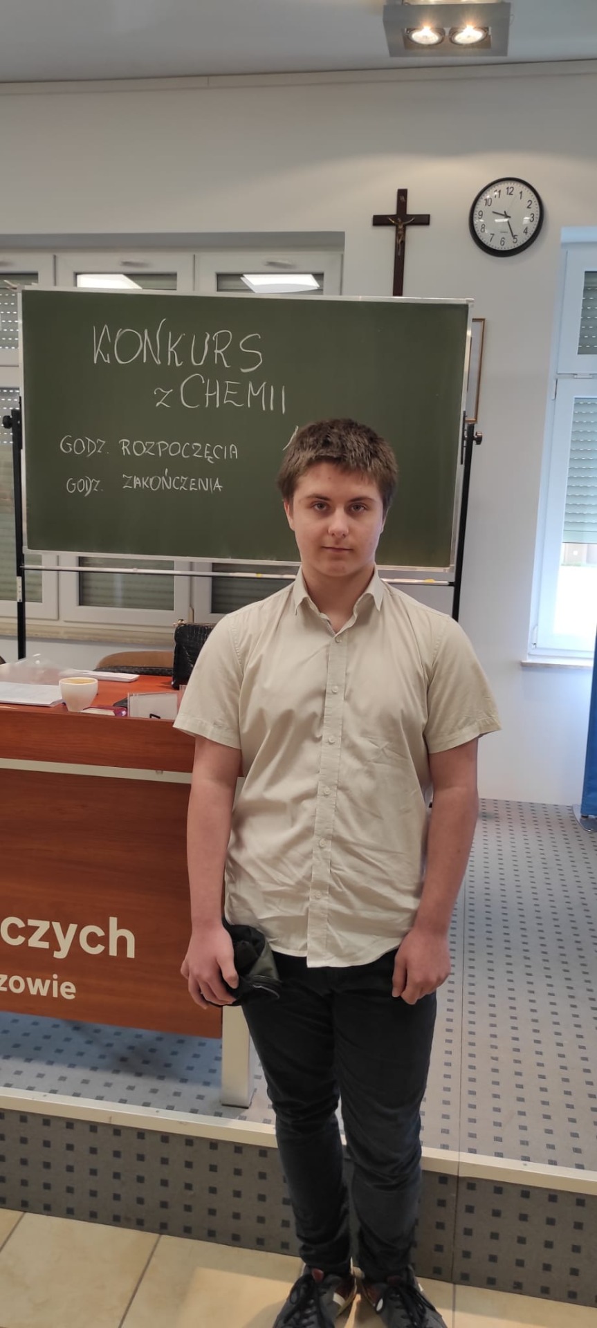 Na zdjęciu uczeń klasy VIII stoi na tle tablicy z napisem Konkurs z chemii.